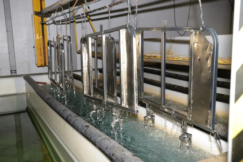 Piezas metálicas sometidas a un proceso de galvanoplastia en bastidores dentro de un tanque de galvanoplastia.