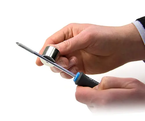 Pessoa deslizando um ímã de neodímio ao longo da haste de uma chave de fenda em uma direção para magnetizá-la.